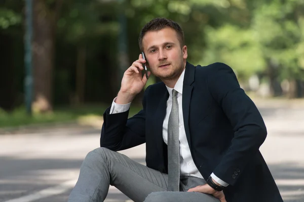 Молодой бизнесмен на улице на телефоне в парке — стоковое фото