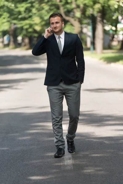 Businessman Walking Outdoors In Park While Using Mobilephone — Stock Photo, Image