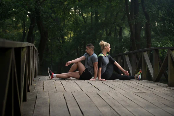 Giovane coppia stretching prima di correre nella foresta boscosa — Foto Stock