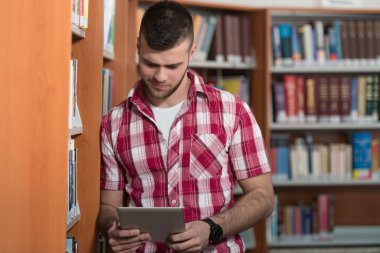 Mutlu erkek öğrenci dizüstü bilgisayar kitaplığı ile çalışma