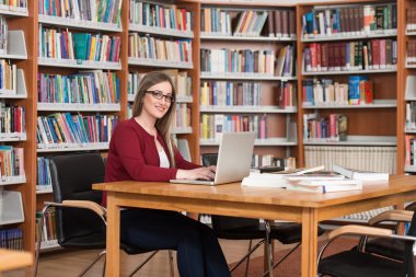 Mutlu kız öğrenci dizüstü bilgisayar kitaplığı ile çalışma