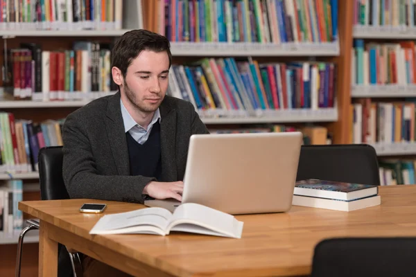 Jeune étudiant utilisant son ordinateur portable dans une bibliothèque — Photo