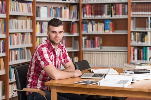 Estudante masculino feliz trabalhando com laptop na biblioteca — Fotografia de Stock