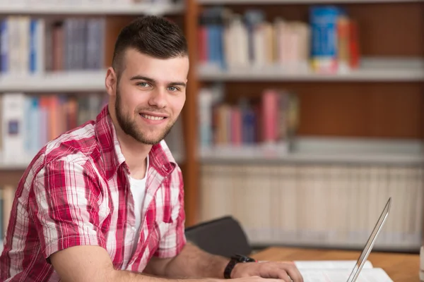 Estudiante masculino feliz trabajando con el ordenador portátil en la biblioteca — Foto de Stock