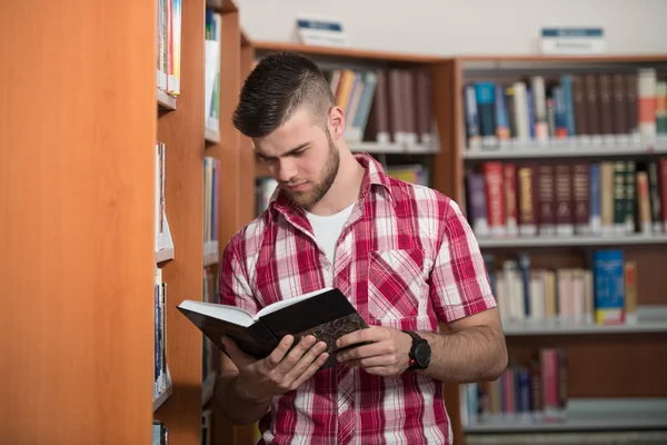 Bonito jovem estudante universitário em uma biblioteca — Fotografia de Stock