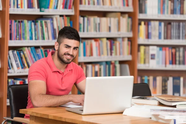 Счастливый студент с ноутбуком в библиотеке — стоковое фото