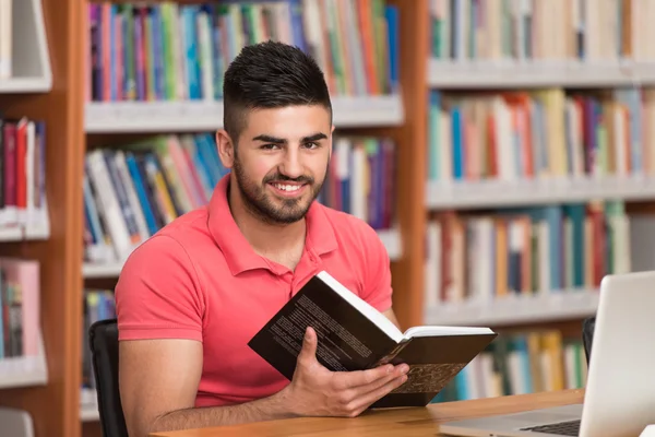 Счастливый студент с ноутбуком в библиотеке — стоковое фото