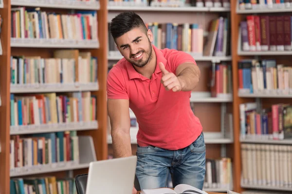 Ung Man i en bibliotek visar tummen upp — Stockfoto