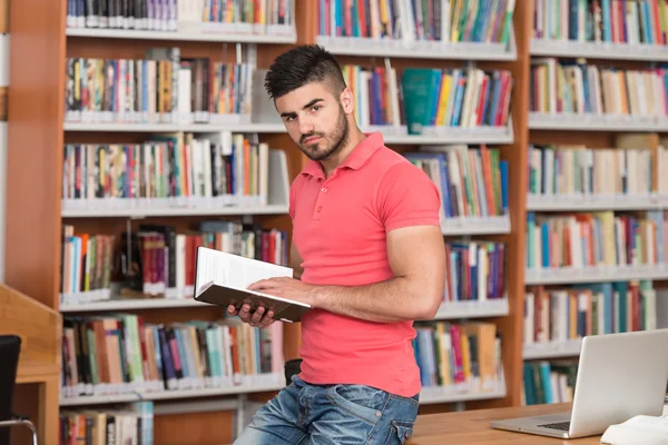 Estudante masculino feliz com livro na biblioteca — Fotografia de Stock