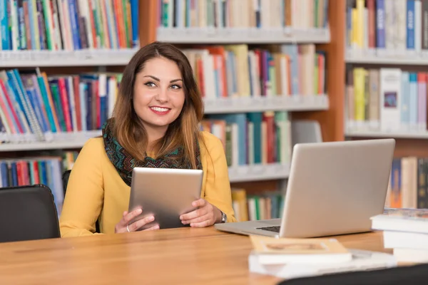 Счастливая студентка с ноутбуком в библиотеке — стоковое фото