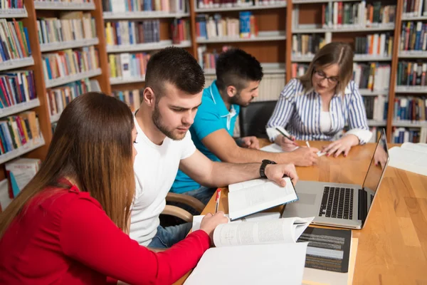 Счастливые студенты, работающие с ноутбуком в библиотеке — стоковое фото