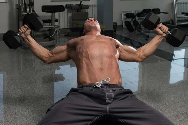 Muskularny mężczyzna robi ćwiczenia na klatkę piersiową z hantlami — Zdjęcie stockowe