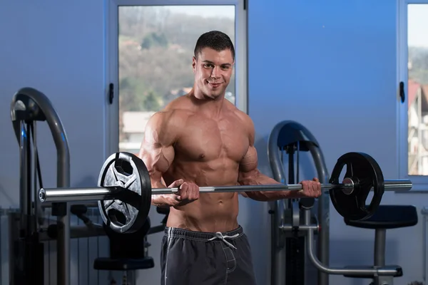 Hombre en el gimnasio ejercitando bíceps con barra — Foto de Stock