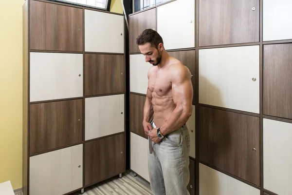 Construtor de corpo mudando de roupa na sala de armário de ginástica — Fotografia de Stock