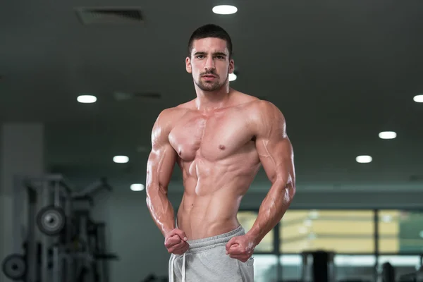 Impresionante culturista mostrando sus músculos y posando en el gimnasio — Foto de Stock