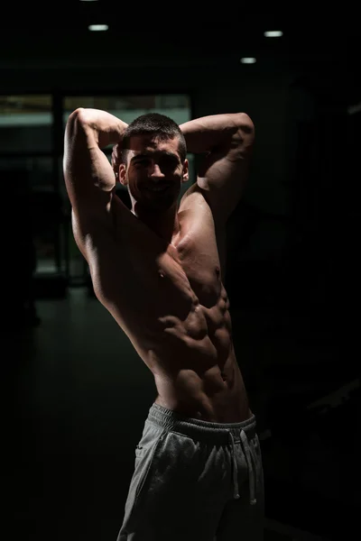 Muscular hombre flexión músculos en oscuro gimnasio —  Fotos de Stock