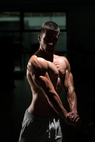 Gespierde Man buigen spieren In donkere sportschool — Stockfoto