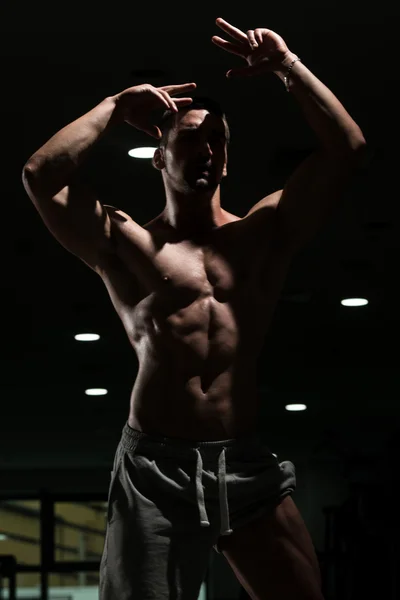 Muscular hombre flexión músculos en oscuro gimnasio — Foto de Stock