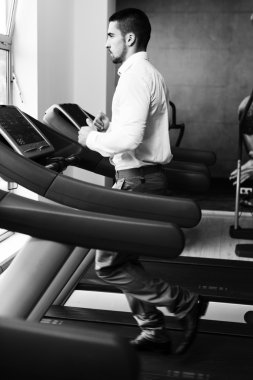 Spor salonunda koşu bandı üzerinde çalışan iş adamı