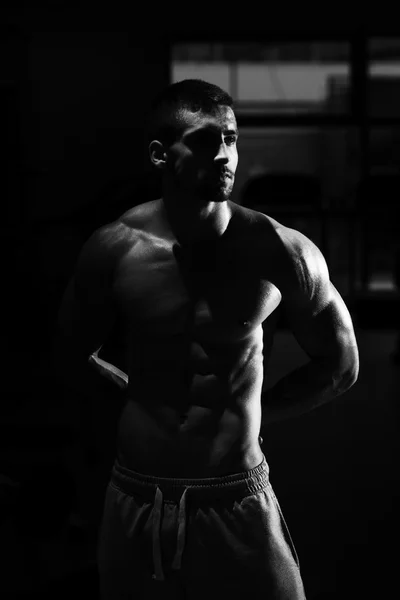 Muscular hombre flexión músculos en oscuro gimnasio — Foto de Stock