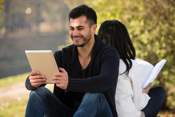 Una pareja mira una tableta y un libro digeriales —  Fotos de Stock