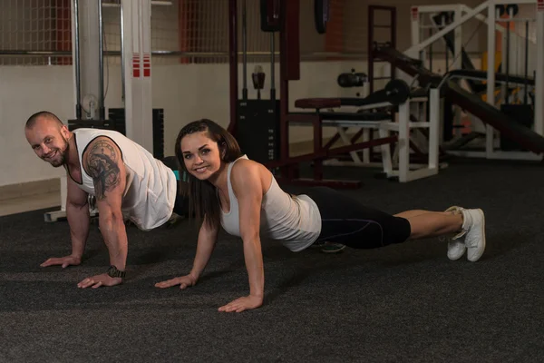 Joven pareja haciendo ejercicio push-up en el gimnasio — Foto de Stock
