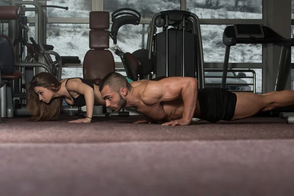 Joven pareja haciendo flexiones en el gimnasio — Foto de Stock