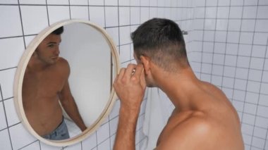 Sakallı adam pamuklu çubukla kulakları temizlerken aynaya bakıyor. 