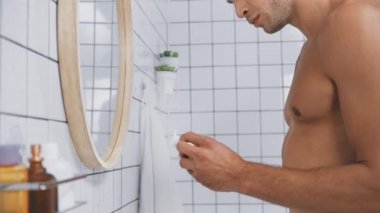 Banyoda diş ipi kullanırken elinde diş ipi tutan üstsüz bir adam. 