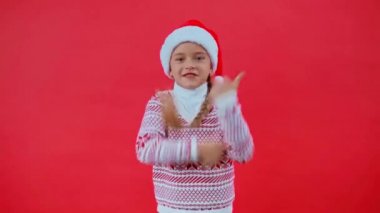 Noel Baba şapkalı ve Noel süveterli kız kırmızıda yalnız dans ediyor.