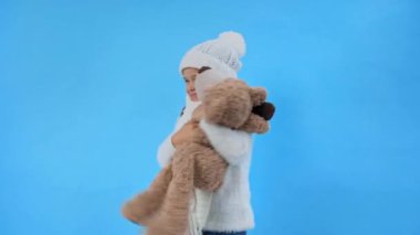 Mutlu kız örülmüş beyaz kışlık kıyafetli ve ayıcığı maviden soyutlanmış