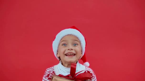 戴着圣诞礼帽 头戴圣诞毛衣 快乐的女孩跳起来 礼物是红色的 — 图库视频影像