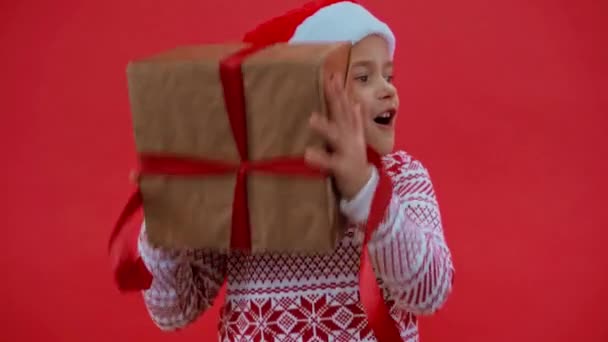 Aufgeregtes Mädchen Weihnachtsmütze Und Weihnachtspullover Schüttelt Geschenkbox Isoliert Auf Rot — Stockvideo
