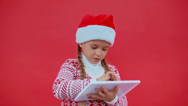 Menina Santa Chapéu Camisola Natal Usando Tablet Digital Isolado Vermelho — Vídeo de Stock
