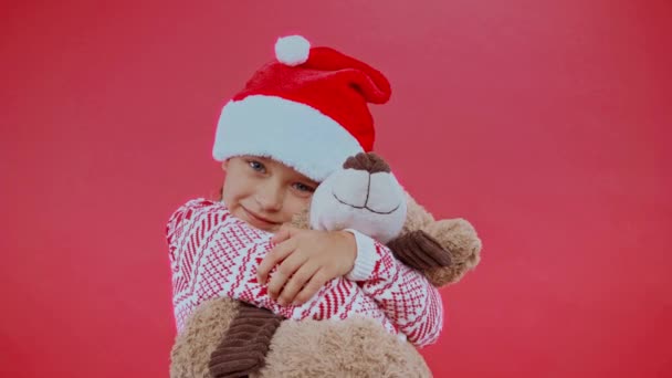 头戴圣诞礼帽 头戴圣诞毛衣 抱着被红色隔离的泰迪熊的女孩 — 图库视频影像