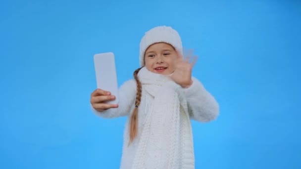 Mädchen Gestricktem Weißen Winteroutfit Winkt Bei Videoanruf Vereinzelt Auf Blau — Stockvideo