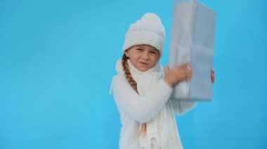 Kışın örülmüş beyaz elbiseli kız mavi üzerine izole edilmiş hediye kutusunu sallıyor.