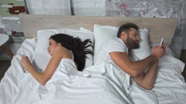 Yatakta uzanan ve akıllı telefonlarda mesajlaşan çiftin yüksek açılı görüntüsü