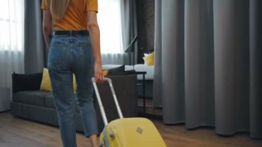 Hasır şapkalı kadın otel odasında bavulla yürüyor.