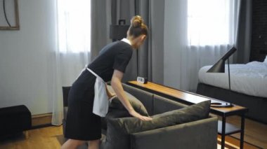 Genç hizmetçi otel odasındaki kanepede yastık ayarlıyor. 
