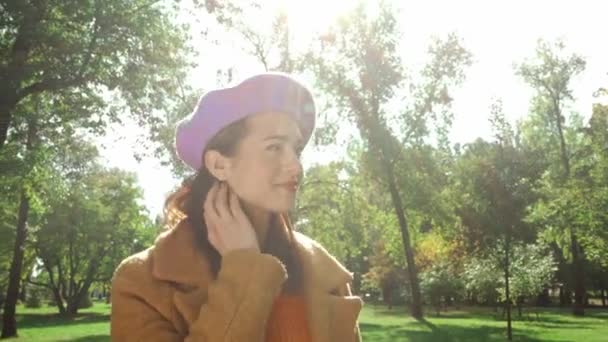 Uśmiechnięta Kobieta Jesiennych Ubraniach Dotykająca Włosów Podczas Spaceru Parku — Wideo stockowe