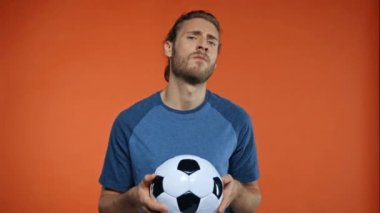 Futbol topu gösteren agresif bir adam turuncu üzerine izole edilmiş bir jest yapıyor.