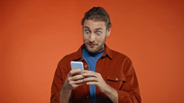 Hombre Emocionado Jugando Teléfono Inteligente Mostrando Gesto Ganar Aislado Naranja — Vídeos de Stock