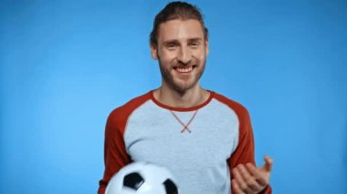 Futbol topu gösteren neşeli adam benimle gel. Maviye saklanmış bir jest yap.