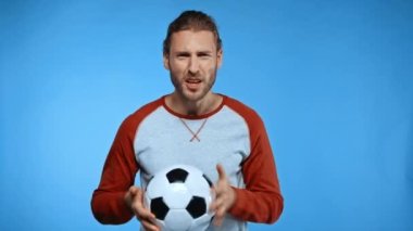 Futbol topundan memnun olmayan bir adam mavi ışıkta el sallıyor ve bağırıyor.