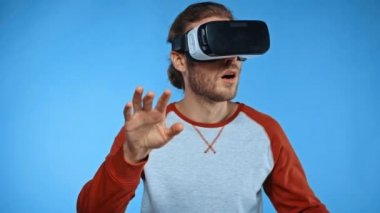 VR kulaklıklı adam mavi bir şeye dokunuyor ve hareket ediyor.