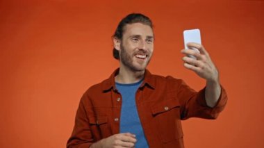 Portakalda izole edilmiş akıllı telefondan görüntülü arama yaparken neşeli adam el kol hareketi yapıyor.