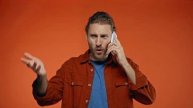 Akıllı telefondan konuşan ve portakalda izole hareket eden hoşnutsuz bir adam.