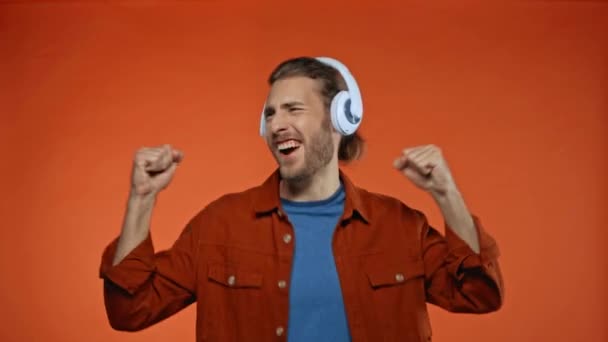 Energiczny Mężczyzna Śpiew Taniec Słuchawkach Odizolowanych Pomarańczowy — Wideo stockowe