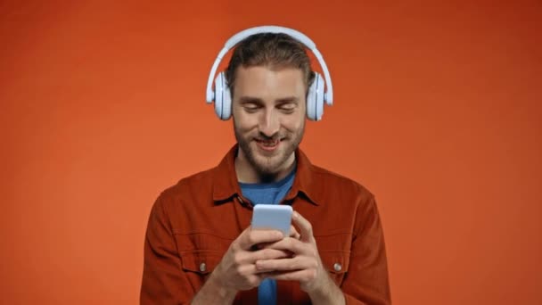 Szczęśliwy Człowiek Słuchawkach Czat Smartfonie Odizolowany Pomarańczowy — Wideo stockowe